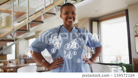 Standing nurse wearing blue scrubs and stethoscope in open-plan clinic, digital icons overlaying Standing nurse wearing blue scrubs and stethoscope in open-plan clinic, digital icons overlaying 139572184