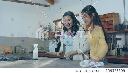 Wiping daughter in yellow top, mother in cardigan at kitchen island, with sprayer and cloth Wiping daughter in yellow top, mother in cardigan at kitchen island, with sprayer and cloth 139572209