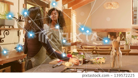 Two women wearing aprons preparing salad on cutting board, pouring drinks in home kitchen, overlay Two women wearing aprons preparing salad on cutting board, pouring drinks in home kitchen, overlay 139572225