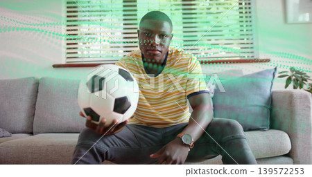Holding soccer ball, man wearing yellow T-shirt leaning on living room sofa, wristwatch visible Holding soccer ball, man wearing yellow T-shirt leaning on living room sofa, wristwatch visible 139572253