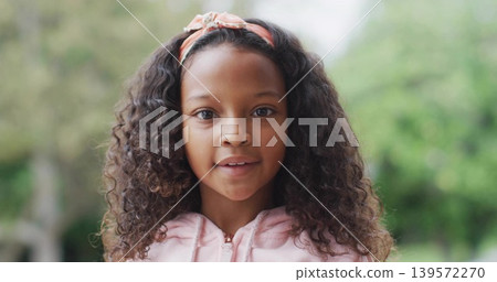 Looking girl with curly hair speaking at park, wearing light pink zip-up hoodie and headband Looking girl with curly hair speaking at park, wearing light pink zip-up hoodie and headband 139572270