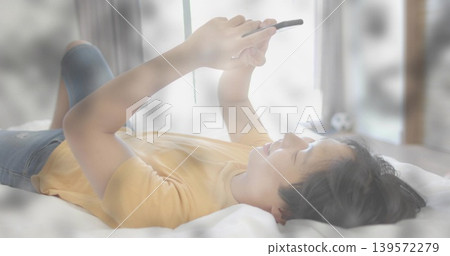 Lying adult Asian man wearing yellow T-shirt and blue jeans, holding tablet above face in bedroom Lying adult Asian man wearing yellow T-shirt and blue jeans, holding tablet above face in bedroom 139572279