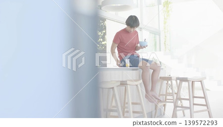 Sitting Asian man in red tee holding bowl and spoon on counter with juice, copy space Sitting Asian man in red tee holding bowl and spoon on counter with juice, copy space 139572293