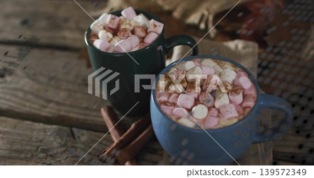 Sitting blue green mugs steaming cocoa on wooden table, with pink marshmallows and cinnamon sticks Sitting blue green mugs steaming cocoa on wooden table, with pink marshmallows and cinnamon sticks 139572349