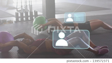 Crunching partners wearing sportswear on gym mat, holding green purple medicine balls with HUD Crunching partners wearing sportswear on gym mat, holding green purple medicine balls with HUD 139572371