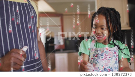 Smiling girl in apron mixing flour in kitchen, adult in striped apron holding cloth, binary overlay Smiling girl in apron mixing flour in kitchen, adult in striped apron holding cloth, binary overlay 139572373