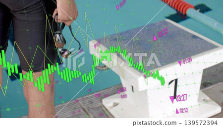 Standing swimmer in black jammer holding goggles by start block poolside, with charts, copy space Standing swimmer in black jammer holding goggles by start block poolside, with charts, copy space 139572394