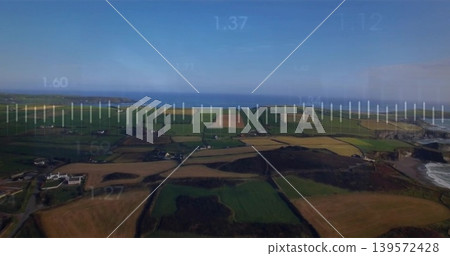 Surveying drone capturing patchwork farmland, hedges, narrow roads over coastal bay, telemetry HUD 139572428