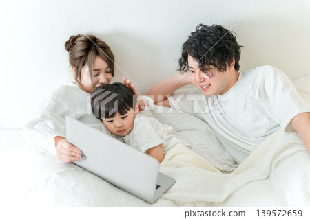 A couple uses a computer to get their son to sleep in the bedroom. A couple uses a computer to get their son to sleep in the bedroom. 139572659
