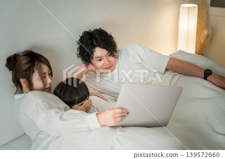 A couple uses a computer to get their son to sleep in the bedroom. A couple uses a computer to get their son to sleep in the bedroom. 139572660