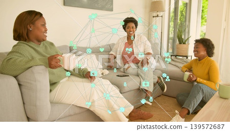 Chatting women in casual clothes sitting on gray sofa at home, holding mugs and smartphone overlay Chatting women in casual clothes sitting on gray sofa at home, holding mugs and smartphone overlay 139572687