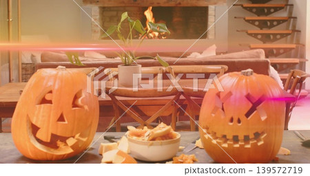 Glowing two carved pumpkins resting on tabletop at home, with bowl of guts and seeds, tools Glowing two carved pumpkins resting on tabletop at home, with bowl of guts and seeds, tools 139572719