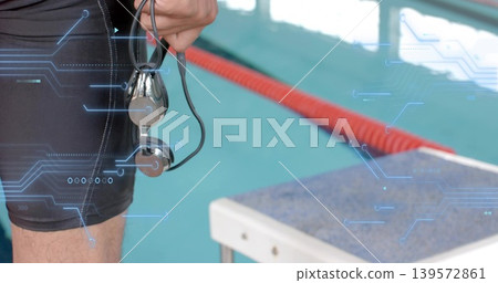 Holding wired earphones, adult male swimmer standing at pool lane with black jammers, copy space 139572861