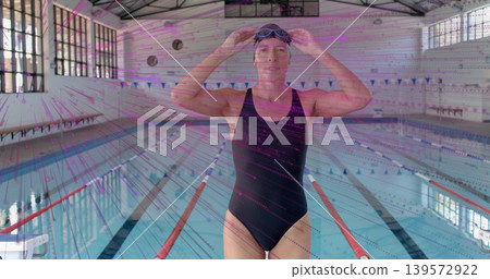 Adjusting swimmer holding goggles in competition pool, wearing black swimsuit and cap, lane-ropes Adjusting swimmer holding goggles in competition pool, wearing black swimsuit and cap, lane-ropes 139572922