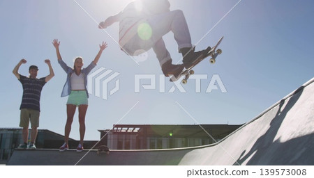 Soaring skateboarder wearing jeans and light top executing trick at ramp, with resting skateboard Soaring skateboarder wearing jeans and light top executing trick at ramp, with resting skateboard 139573008