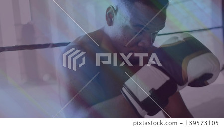 Leaning shirtless male boxer holding white-black gloves by face in ring corner with neon flares Leaning shirtless male boxer holding white-black gloves by face in ring corner with neon flares 139573105
