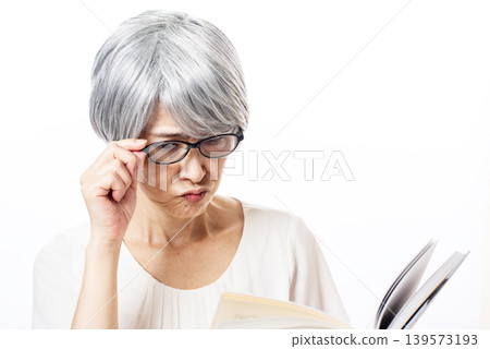 一位戴著黑框老花眼鏡的老婦人正在努力閱讀。 139573193