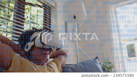 Reclining man wearing white VR headset and yellow striped shirt on sofa in room, binary overlay Reclining man wearing white VR headset and yellow striped shirt on sofa in room, binary overlay 139573380