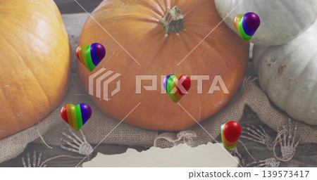 Showing large orange pumpkin resting on burlap on wood, with rainbow-heart balloons, skeleton hands Showing large orange pumpkin resting on burlap on wood, with rainbow-heart balloons, skeleton hands 139573417