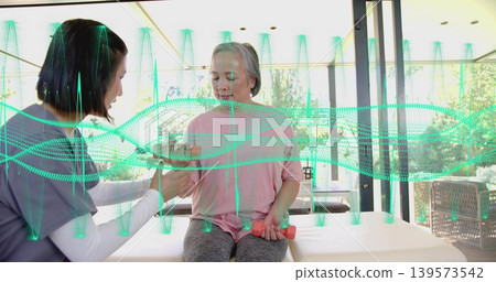 Therapist assisting woman in pink top, grey pants lifting pink dumbbells by glass walls, waveform Therapist assisting woman in pink top, grey pants lifting pink dumbbells by glass walls, waveform 139573542