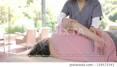 Helping therapist in gray scrubs guiding patient in pink top on padded table near windows, overlay Helping therapist in gray scrubs guiding patient in pink top on padded table near windows, overlay 139573543