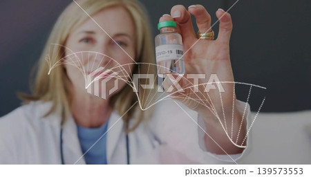 Senior female doctor holding COVID-19 vial in clinic, with white lab coat and DNA helix overlay Senior female doctor holding COVID-19 vial in clinic, with white lab coat and DNA helix overlay 139573553