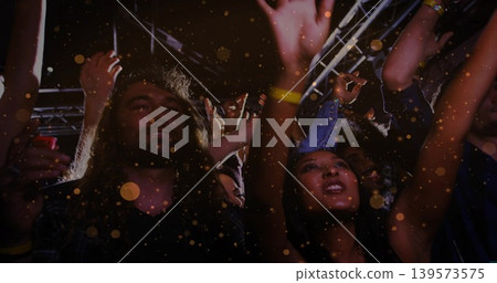 Cheering concert crowd raising hands near lighting rig, showing wristbands and casual tees Cheering concert crowd raising hands near lighting rig, showing wristbands and casual tees 139573575