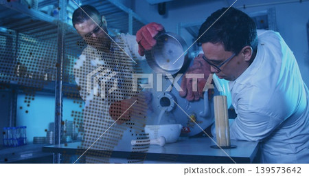 Leaning lab-coated man steadying bowl receiving Dewar vapor at lab bench, red gloves, copy space Leaning lab-coated man steadying bowl receiving Dewar vapor at lab bench, red gloves, copy space 139573642
