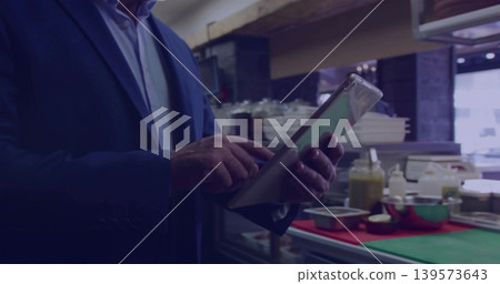 Tapping man in dark blazer checking tablet at kitchen prep counter, green cutting board present Tapping man in dark blazer checking tablet at kitchen prep counter, green cutting board present 139573643