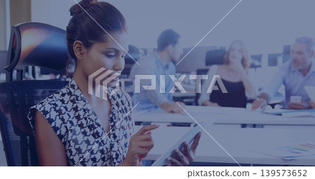 Tapping adult woman using tablet in office, wearing patterned blouse and bun, seated in mesh chair Tapping adult woman using tablet in office, wearing patterned blouse and bun, seated in mesh chair 139573652