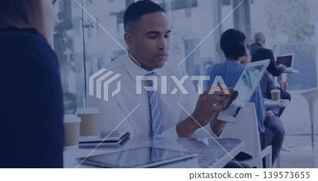 Holding tablet, man wearing white shirt and striped tie tapping screen at cafe with laptops, cups Holding tablet, man wearing white shirt and striped tie tapping screen at cafe with laptops, cups 139573655