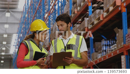 Warehouse staff checking stock in aisle, wearing yellow hard hat, holding tablet and paperwork Warehouse staff checking stock in aisle, wearing yellow hard hat, holding tablet and paperwork 139573693