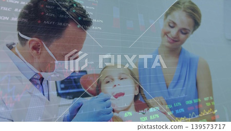 Examining dentist leaning over child in dental clinic, using mirror, blue gloves and market charts Examining dentist leaning over child in dental clinic, using mirror, blue gloves and market charts 139573717
