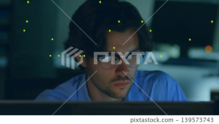 Focusing adult male in light-blue shirt and eyeglasses at desk, studying monitors with marker dots Focusing adult male in light-blue shirt and eyeglasses at desk, studying monitors with marker dots 139573743