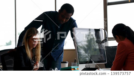 Pointing three colleagues in office wearing work attire discussing graphs on monitor, showing phone Pointing three colleagues in office wearing work attire discussing graphs on monitor, showing phone 139573757