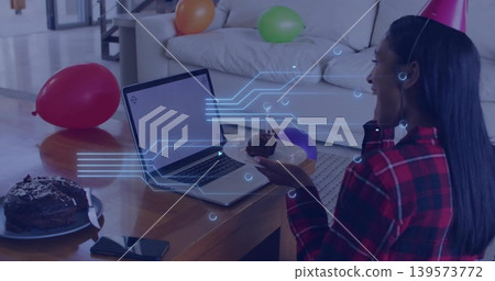 Holding cake, woman in plaid shirt, party hat, sitting in living room, with laptop, copy space Holding cake, woman in plaid shirt, party hat, sitting in living room, with laptop, copy space 139573772