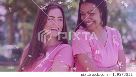 Smiling two women wearing pink vneck tees posing in park, showing ribbon pins and snowflakes Smiling two women wearing pink vneck tees posing in park, showing ribbon pins and snowflakes 139573831