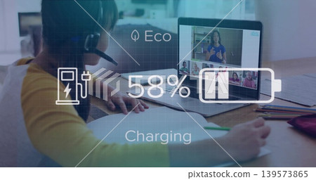 Writing girl in yellow top headset leaning at home table, laptop showing call 58% charging overlay 139573865