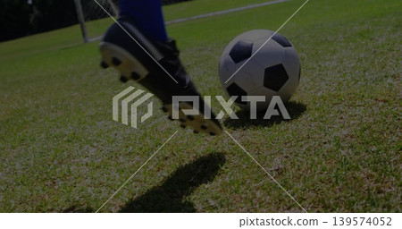 Kicking player swinging black cleat and blue sock at b and w ball on grass, goalpost, copy space Kicking player swinging black cleat and blue sock at b and w ball on grass, goalpost, copy space 139574052