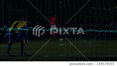 Kicking red kit player approaching soccer ball on night pitch with goal net, teal analytics overlay 139574055