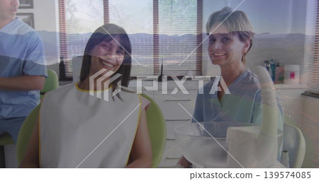 Smiling patient in white bib yellow trim, sitting in green dental chair, staff in blue scrubs Smiling patient in white bib yellow trim, sitting in green dental chair, staff in blue scrubs 139574085
