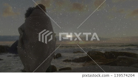 Standing woman wearing fur-trimmed blanket gazing toward low sun over rocky shore, copy space Standing woman wearing fur-trimmed blanket gazing toward low sun over rocky shore, copy space 139574204
