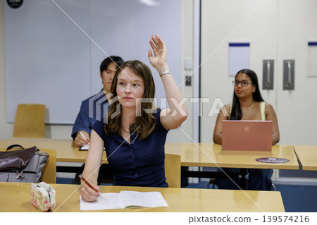 一位年輕女子在教室裡聽課,邊聽邊舉手提問。 一位年輕女子在教室裡聽課,邊聽邊舉手提問。 139574216