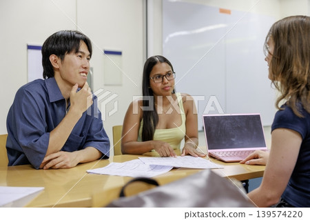 A young man and woman discuss while looking at documents; a scene from a learning and business meeting. A young man and woman discuss while looking at documents; a scene from a learning and business meeting. 139574220