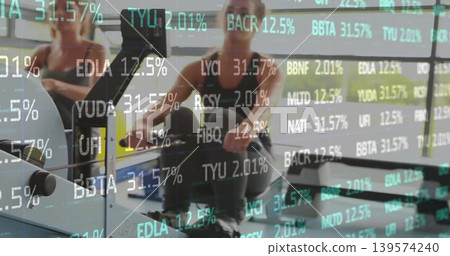 Rowing women pulling handles on ergometers in gym, in dark athletic wear with green ticker overlay Rowing women pulling handles on ergometers in gym, in dark athletic wear with green ticker overlay 139574240