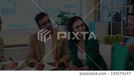 Speaking center woman in green cardigan leading team meeting in small office, notebooks teal folder Speaking center woman in green cardigan leading team meeting in small office, notebooks teal folder 139574247