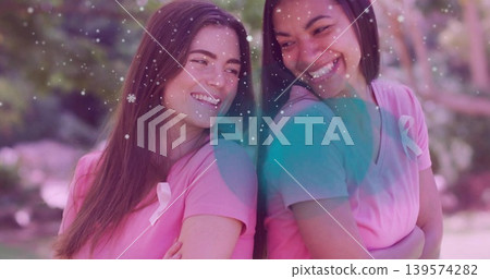 Smiling two women leaning back-to-back in park, wearing matching pink shirts with ribbons Smiling two women leaning back-to-back in park, wearing matching pink shirts with ribbons 139574282