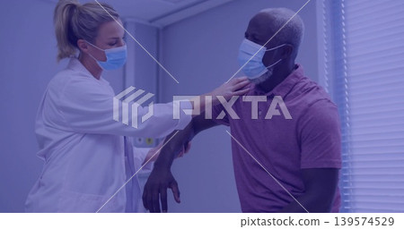 Examining female doctor supporting male patient raising arm in exam room, wearing white coat, masks Examining female doctor supporting male patient raising arm in exam room, wearing white coat, masks 139574529