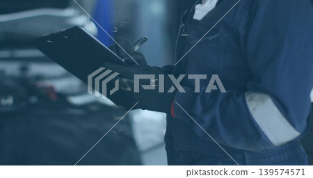 Checking woman mechanic writing on clipboard with pen in garage, open hood, coveralls, gloves Checking woman mechanic writing on clipboard with pen in garage, open hood, coveralls, gloves 139574571