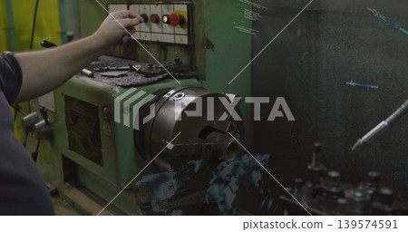Reaching machinist in dark shirt pressing panel button on lathe in workshop with chuck, copy space Reaching machinist in dark shirt pressing panel button on lathe in workshop with chuck, copy space 139574591